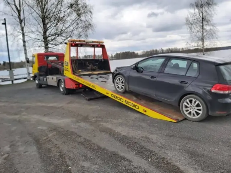Tiiholan Tokan hinausauto lastaa tummaa henkilöautoa lavalleen tien varressa